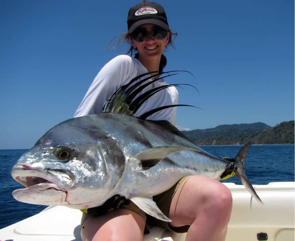 Smiling lady angler holding a Panama trophy roosterfish fish with Isla Parida in the background