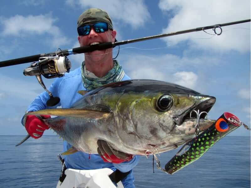 SFPIL angler with his fishing rod in mouth while holding yellowfin tuna that has lure dangling from its mouth