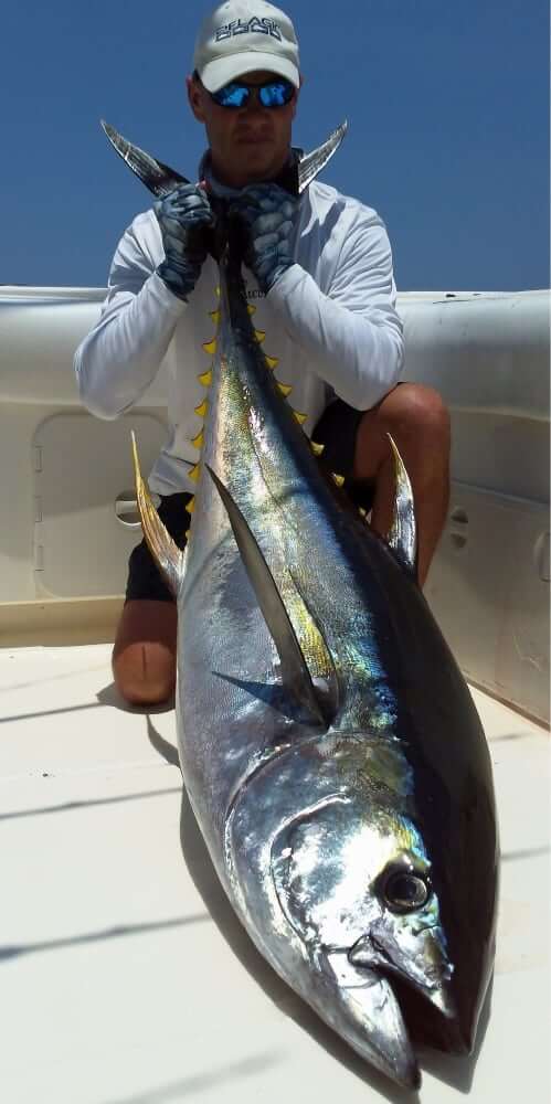 Serious angler kneeling on deck of T.O.P. CAT, holding tail of large yellowfin tuna