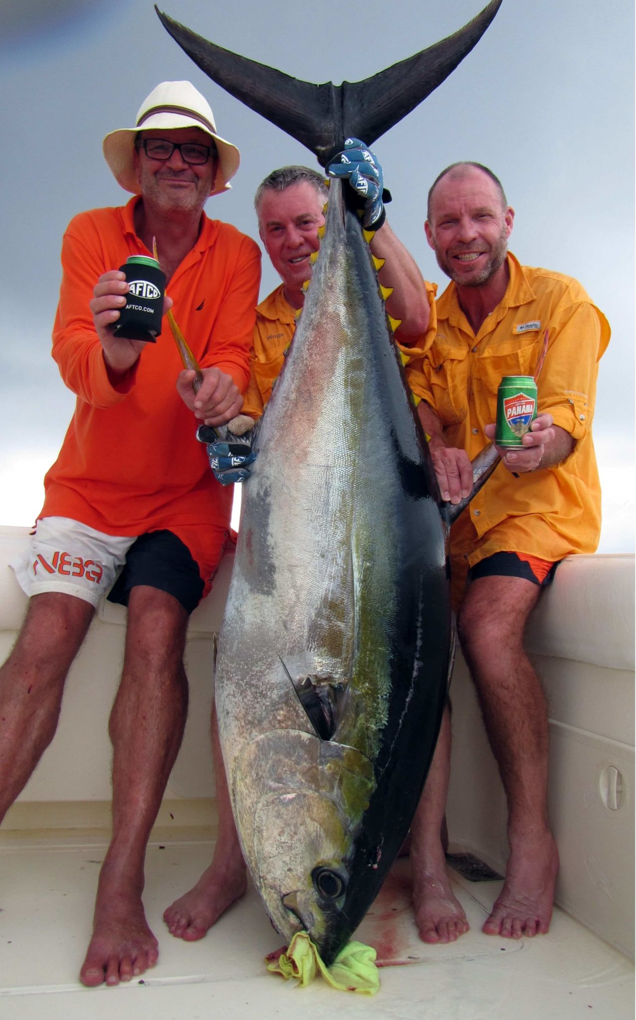 Three anglers holding 230 pound yellowfin tuna, smiling with beers