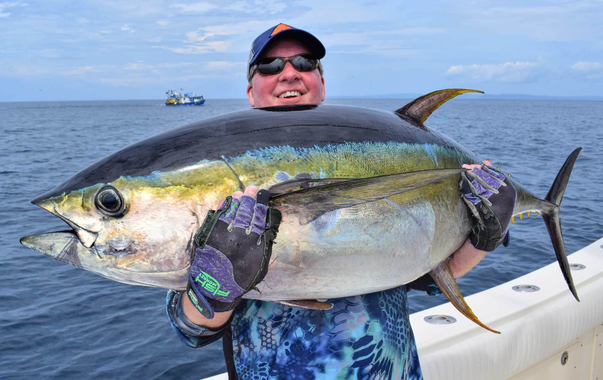 Angler holding large tuna with fishing boat in background