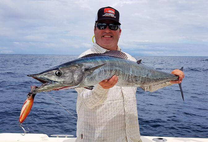 Angler posing with a wahoo, popper hanging from mouth.