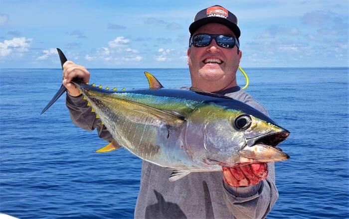angler with sunglasses posing with small yellowfin tuna...