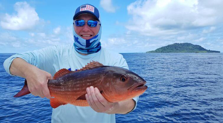 angler holding small Mullet Snapper. Isla Montuosa, Panama in background.