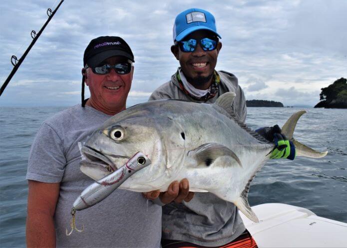 Mate holding Jack Crevalle with popper in mouth with smiling angler in background.