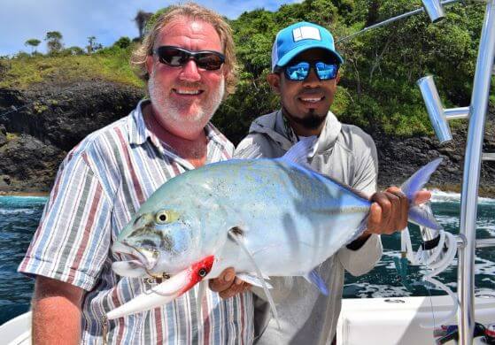 Mate holding Bluefin Trevally with lure in mouth. A Panama island in the background