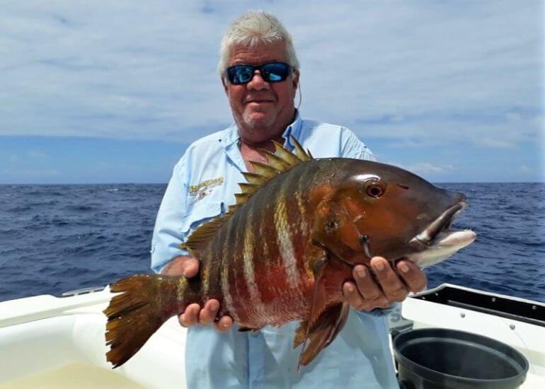 angler holding Mexican Barred Snapper. Panama coastline in background