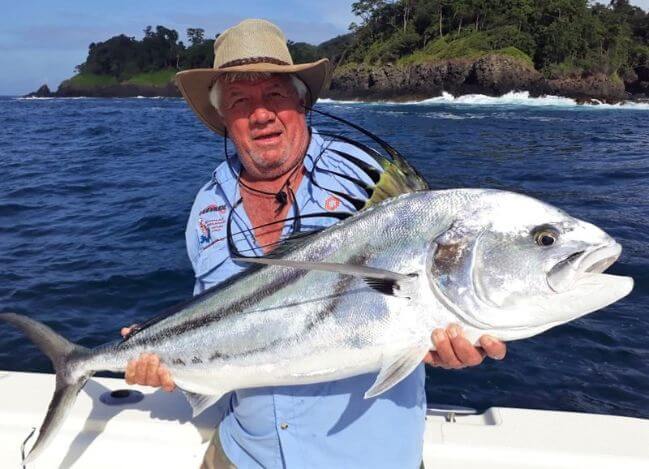 angler posing with roosterfish. Waves and rocks in the background