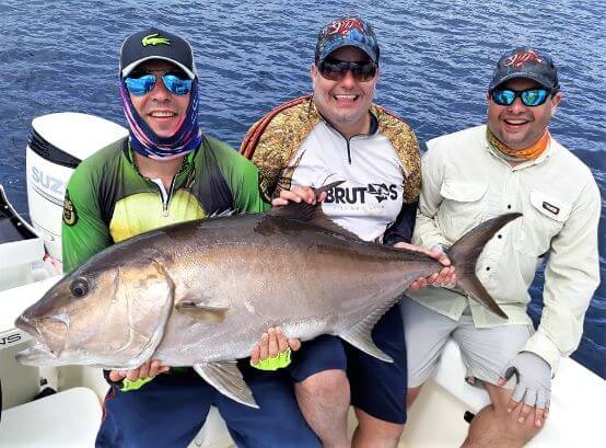 Three smiling anglers posing with amberjack