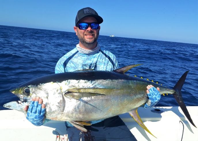 Angler holding 60 pound yellowfin tuna with commercial fishing boat in background