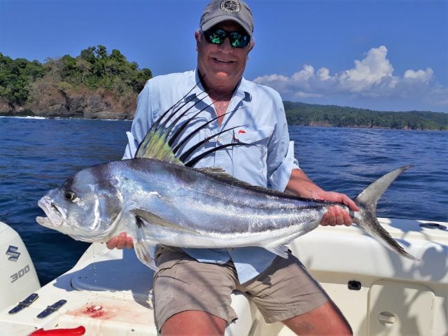 Smiling angler holding small roosterfish with Isla Parida in the background
