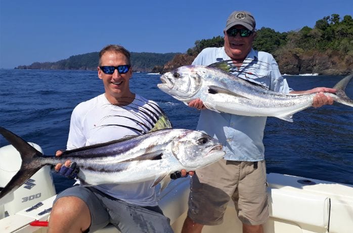 Smiling anglers holding two small roosterfish with Isla Parida in the background