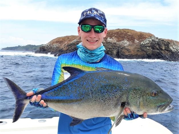 Junior angler posing with Bluefin Trevally  Waves breaking on rocks in background