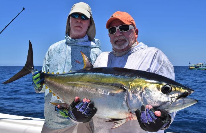 two anglers holding small yellowfin tuna with fishing panga in background
