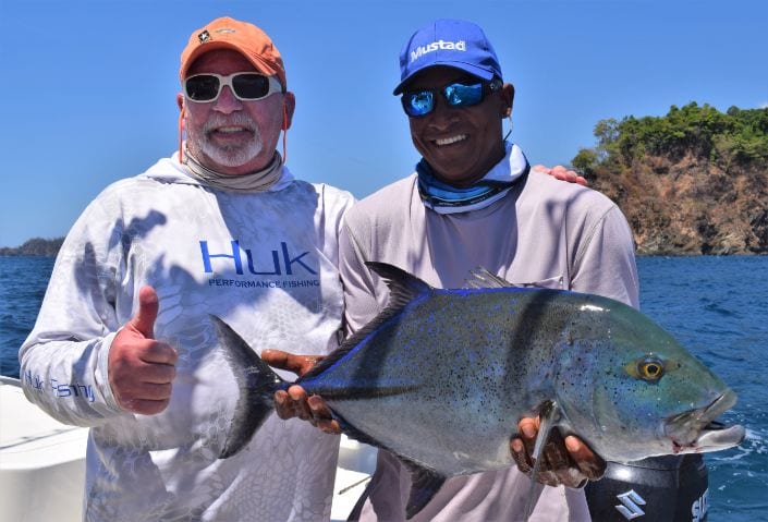 Mate holding Bluefin Trevally while angler gives thumbs up sign