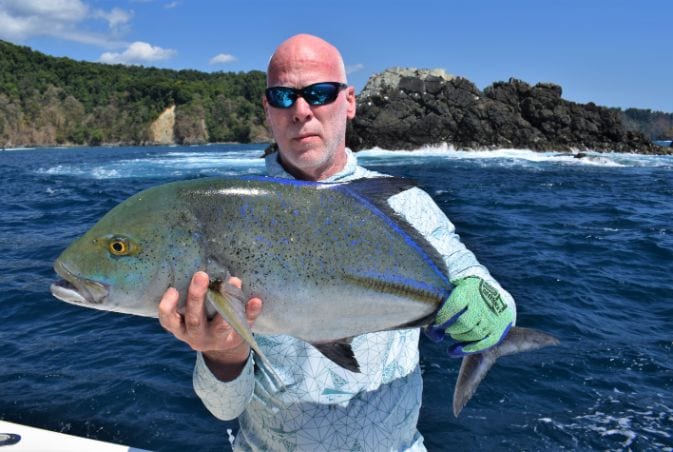 Angler holding Bluefin Trevally with Isla Parida in background