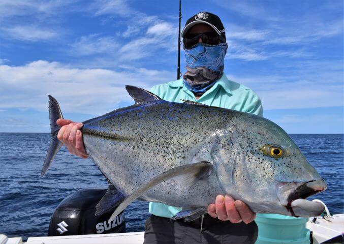 angler holding Bluefin Trevally while posing for picture