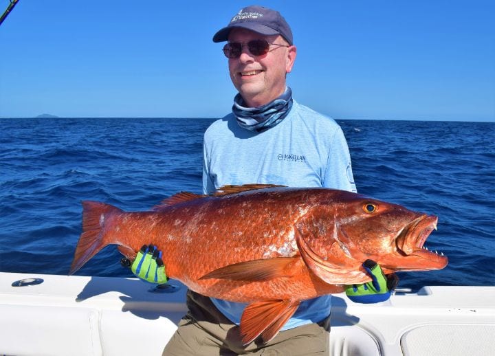 Smiling client holding cubera snapper with Isla Montousa in the background