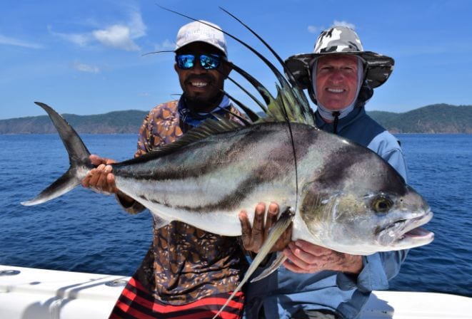 Mate and angler holding roosterfish with Isla Parida in background
