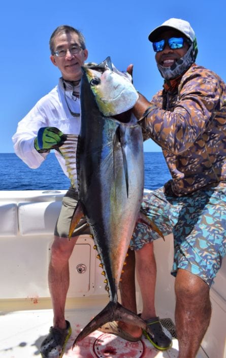 Mate lifting yellowfin tuna for smiling angler