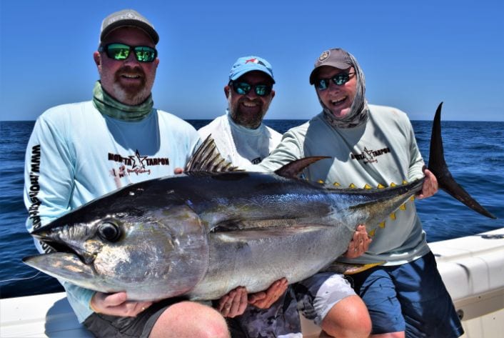 3 anglers sitting on gunnel of a World Cat holding large yellowfin tuna