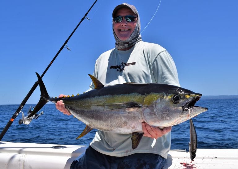Angler holding small yellowfin tuna with lure hanging from the fishes mouth