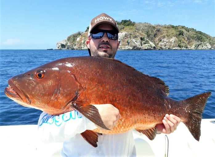 Smiling client holding cubera snapper with Isla Montousa in the background