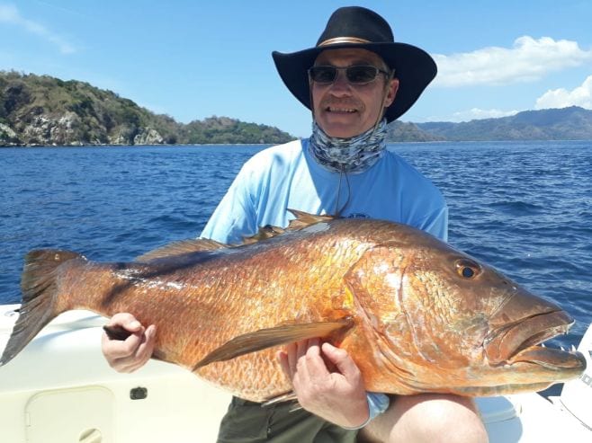 Smiling client holding cubera snapper with Isla Parida in the background