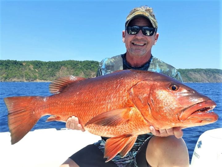 angler posing with cubera snapper and Isla Parida in background