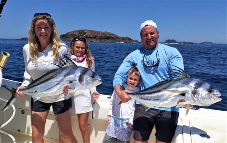 Family posing with roosterfish with small island in the background