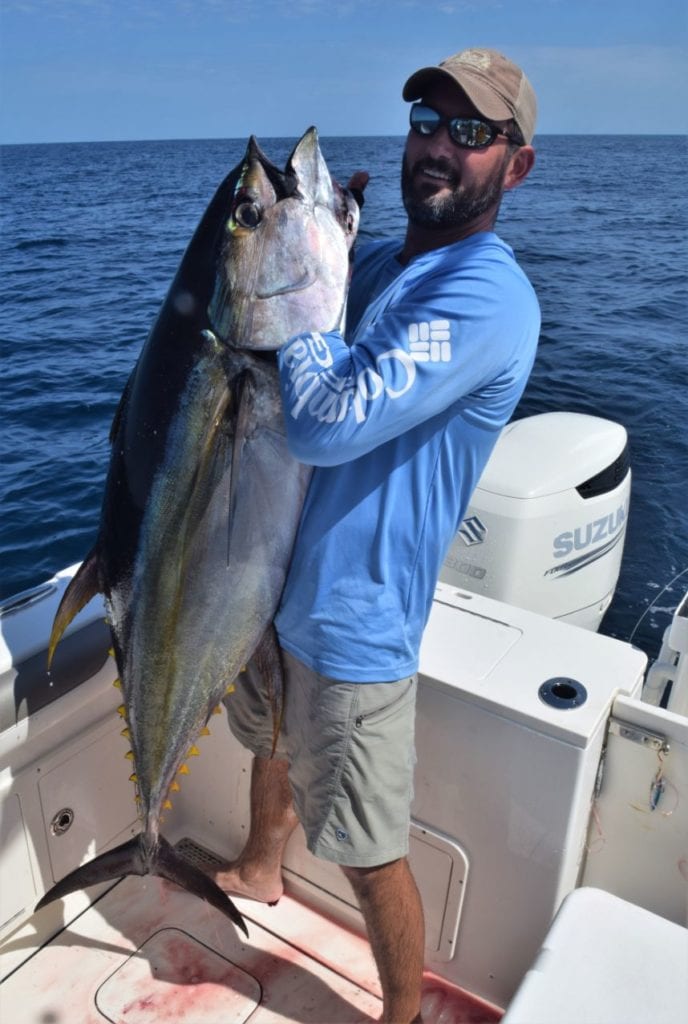 Angler lifting a large yellowfin tuna by the gills.