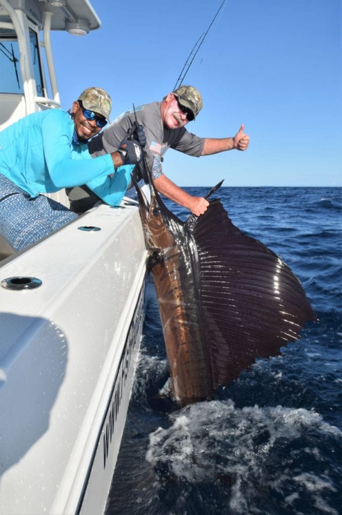 Angler with thumb up sign, whil mate holds sailfish for release alongside World Cat