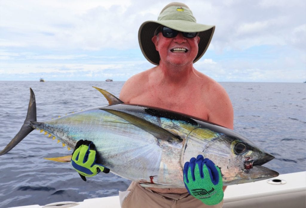 Angler with big hat posing with small yellowfin tuna. Two fishing boats in the background