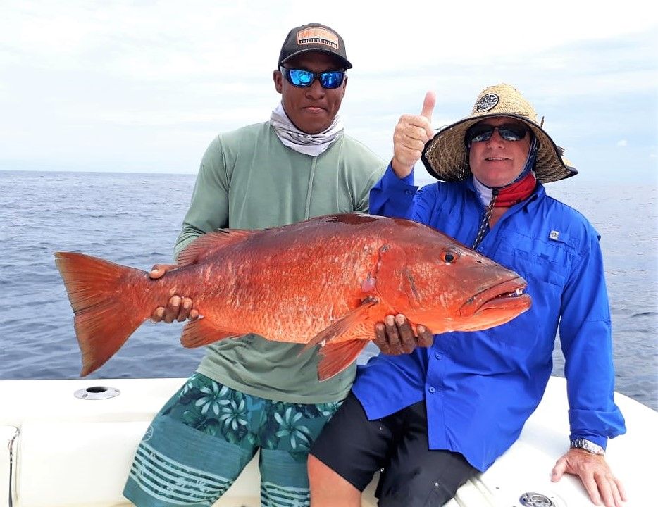 Angler with thumbs up, posing with cubera snapper held by mate