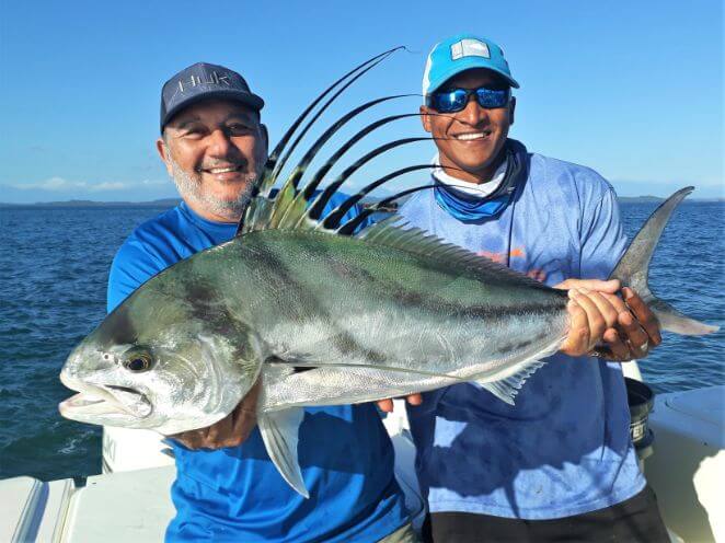 Mate holding roosterfish for smiling angler in picture pose