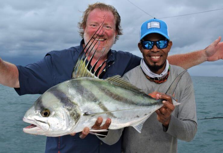 Mate holding roosterfish for angler with out-spread arms.