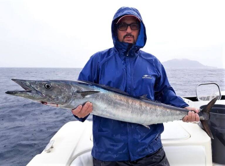 Wahoo being held by puss faced angler for photo op. Isla Montuosa, Panama in background.